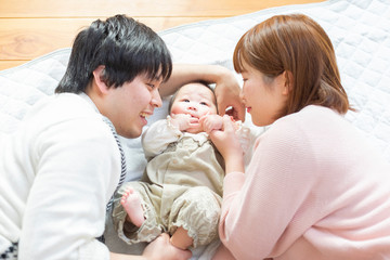 Fototapeta na wymiar 赤ちゃんを中心に寝転ぶ幸せそうな父と母