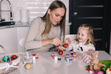 Obraz na płótnie Canvas Happy easter. Young mother and her daughter painting Easter eggs. Happy family preparing for Easter.