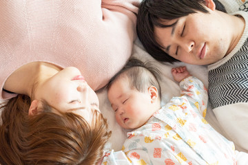 Fototapeta na wymiar 赤ちゃんを中心に昼寝をする幸せそうな父と母