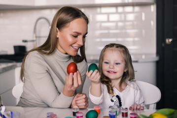 Obraz na płótnie Canvas Mother and small daughter with easter eggs and easter basket in the kitchen ready for Easter
