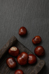 Fresh chestnuts on dark stone background. Pile of fresh chestnuts ready to roast shot over black antique background. Top view. 