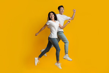 Fototapeta na wymiar Happy asian couple running fast over yellow background