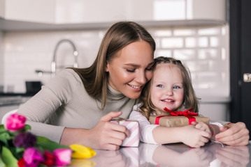 Obraz na płótnie Canvas Smiling mom giving excited daughter present on her birthday. Happy single mother and curious child girl opening pink gift box together. Cute kid receiving holiday gift from mommy concept