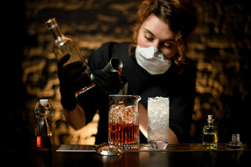 Lady bartender pours alcoholic drink into large glass with ice.