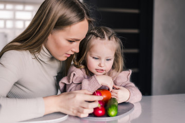 Fototapeta premium Mother and little girl slicing vegetables in the kitchen preparing a salad. Cook at home.