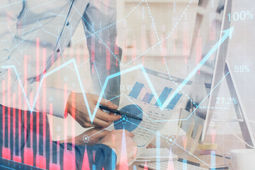 Double exposure of chart with businessman typing on computer in office on background. Concept of hard work.