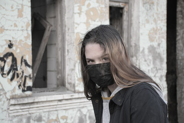 Teenager girl in a black medical mask, on the background of an abandoned post-apocalyptic building. Consequences of COVID-19 Coronavirus protection. After a pandemic