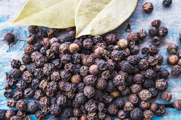 Black pepper and bay leaves are scattered on blue boards.