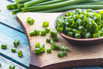 Fresh green onion chopped and lies on a bowl on a chopping board on a background of blue boards.