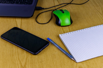 Laptop with mouse, smartphone, notebook and pen on a desk. Working at home and business concept