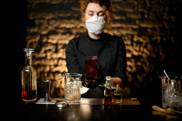 young woman at bar holds prepared cold cocktail in her hands