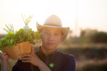 Portrait young asian man smiling harvest and picking up fresh organic vegetable garden in basket in...