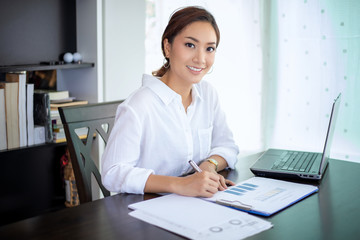 Beautiful Asian business women checking document and using notebook for working at home