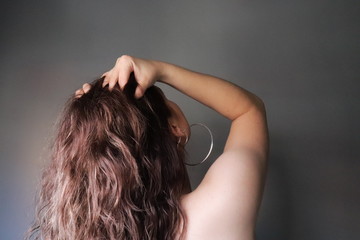 mujer de espaldas desnuda con las manos sobre su cabeza y pendientes de aro