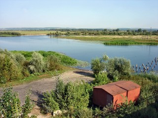 A wide river in the late sunny summer morning. There's an old bridge in the river.
