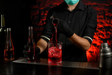 Bartender pours alcoholic drink into large glass with ice.