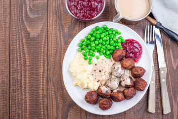 Traditional swedish meatballs served with mashed potato, green peas, cream sauce and cranberry jam, on a plate, horizontal, copy space, top view