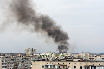 Thick black smoke rises above the city and residential buildings. Fire in the city