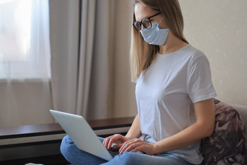 Young woman in medical mask works from home during self isolation and quarantine. Work online and stay at home.