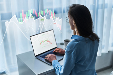 Young modern business woman entrepreneur analyzes and studies a changing chart of stock trade and...