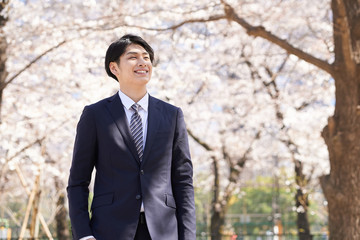 桜を背景に笑顔で立つ日本人男性ビジネスマン