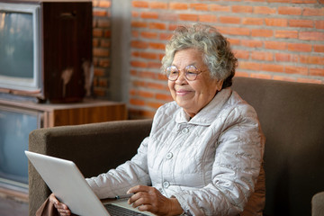 Senior Asian Woman Sit on sofa spend free time at home using social networks having fun chatting...