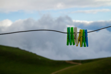 Colourful clothes pegs hanging on washing line with green and cloud background