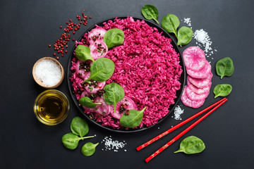 Pink rice (rice with beetroot juice) with radish and spinach leaves in a black plate. Near olive...
