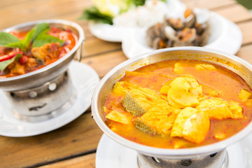 Thai soup salmon fish spicy sour soup wih slice bamboo shoots serve in bowl  put near other foods on wood table