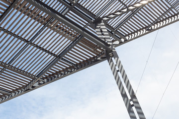 Angled view of metal and wood overhead shade structure on a very sunny day, blue sky and clouds, horizontal aspect