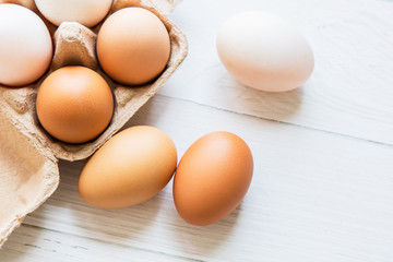 Brown and white organic chicken eggs in a brown paper box placed on a white wooden table. Eggs provide protein, suitable for health lovers.