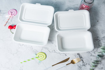 Biodegradable, environmentally friendly disposable fast-food box, set against a marble backdrop, with lollipops and cutlery. Environmentalists love to use it