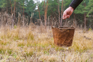 Rusty bucket in human hand on forest background. Trash in the forest. Environmental disaster.