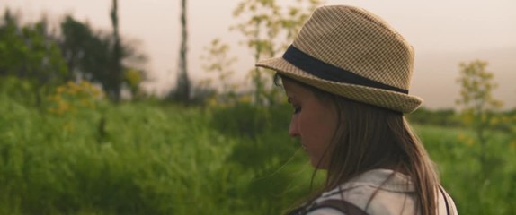 A young girl with backpack and a hat taking pictures of landscape and nature with vintage camera at sunset. CLOSE UP, SLOW MOTION, SHALLOW DOF. Adventure, lifestyle concept. BMPCC 4K 