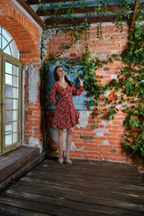 beautiful girl in a red dress sits on a windowsill by the window