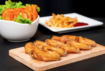 fast food , french fries and fried chicken , with green salad, tomatoes on dark table