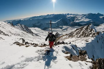 Fotobehang man with ski equipment rises on snowy mountain. © fesenko