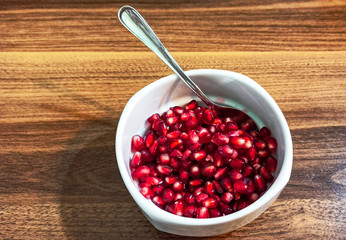 Group of fresh red pomegranate seeds isolated on the white cup with wooden background.