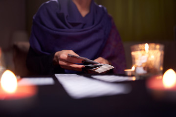 Close-up of woman fortuneteller's hands with cards at table with candles