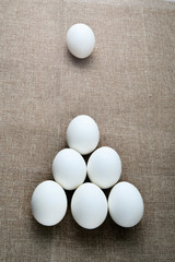 A background made of seven white eggs in a triangle pyramid billiard position on a canvas brown tablecloth vertical.