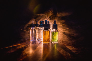 Smoke clouds and vape liquid bottles on dark background. Light effects. Useful as background or...