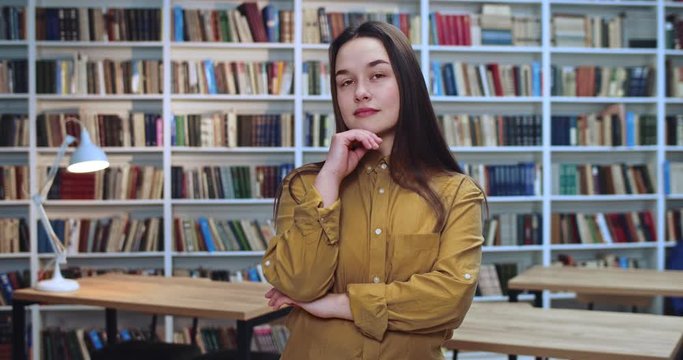 Portrait of toughtful brunette student with long awesom blach hair thinking in library.