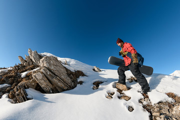Close-up of snowboarder man on top of rocky snowy mountain.