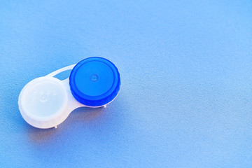 The contact lens container is open on a blue background. Close-up and soft focus.