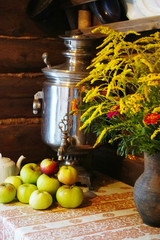 clay vase with wildflowers, a samovar and garden apples on the table