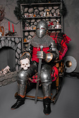 Young knight in armor 14th century with a sword in one hand and a skull in the other hand, sitting...