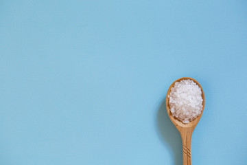 Coarse sea salt in a wooden spoon on a blue background. Ingredient for cooking and spa treatments.