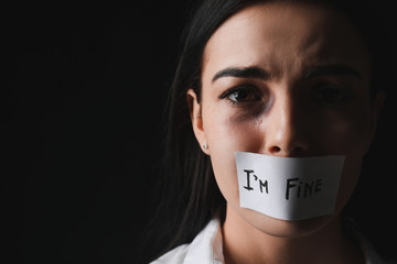 Scared female victim with taped mouth on dark background. Concept of violence