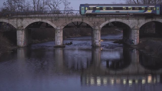 Train is going over the bridge. Reflection of the passing train in the river.