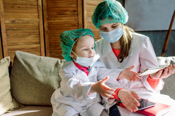 Two cute children play doctor and hospital using stethoscope. girl in uniform of a doctor and in face mask. Coronavirus concept, covid-19.Friends girls having fun at home or preschool.